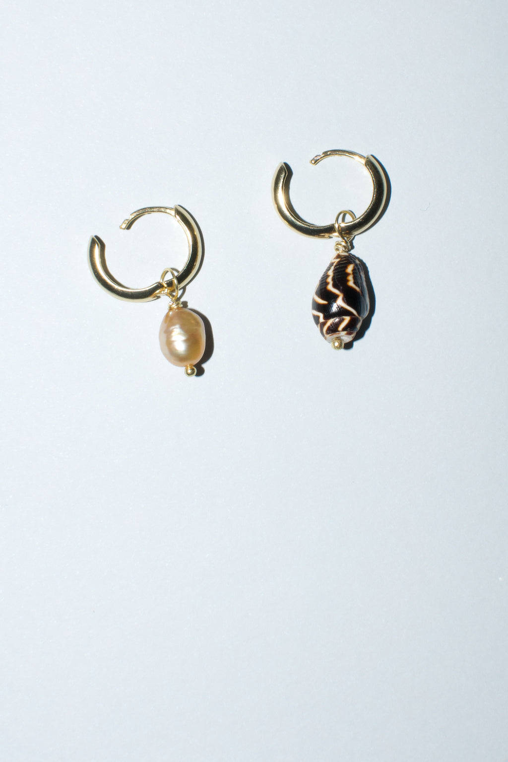 Mismatched hoop earrings by Anouk Gania, one featuring a gold freshwater pearl and the other a pyrene shell. Hoop is open to show click clasp system.