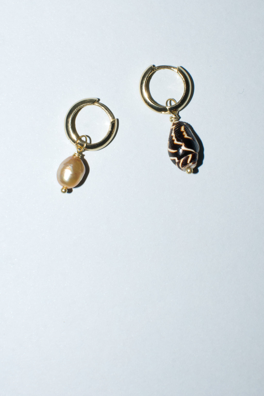 Mismatched hoop earrings by Anouk Gania, one featuring a gold freshwater pearl and the other a pyrene shell.